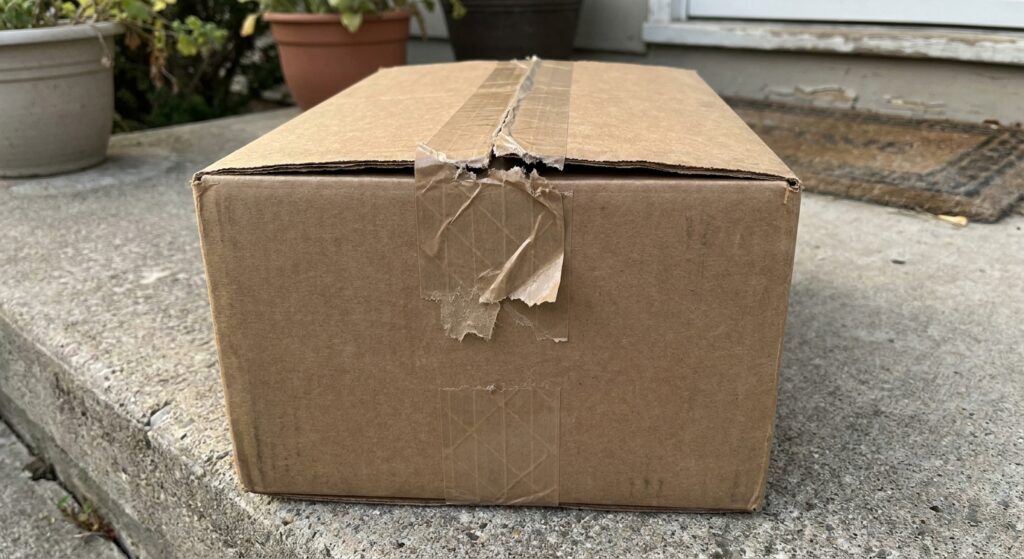 A cardboard shipping box with its tamper-evident security tape peeled back and resealed unevenly