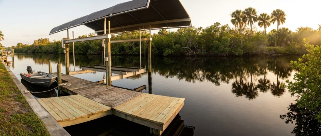 A residential boat lift and wooden dock on a Southwest Florida canal at golden hour, with a small boat tied alongside